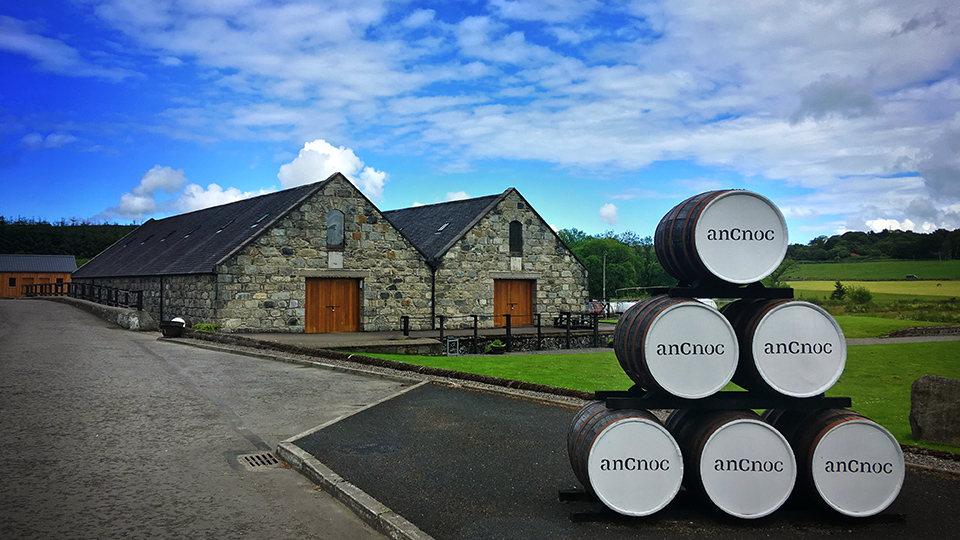 La distillerie de whisky anCnoc (Knockdhu) avec ses bâtiments en pierre traditionnels et des fûts de chêne empilés à l'extérieur.