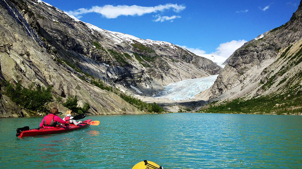 Une famille en kayak sur un lac glaciaire aux eaux turquoise, pagayant vers la langue du glacier Nigardsbreen.