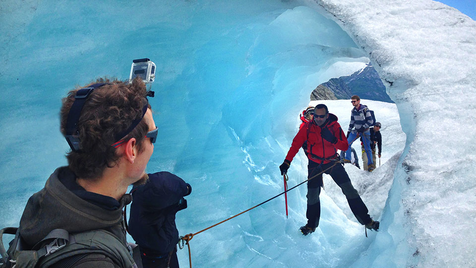 Des randonneurs équipés de crampons explorant l'intérieur d'une grotte de glace aux parois bleues translucides sur le glacier Jostedalsbreen.
