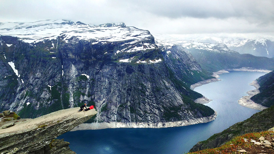 Un randonneur assis au bord de la formation rocheuse de Trolltunga, surplombant un fjord aux eaux bleues profondes en Norvège.