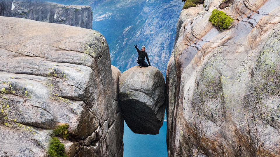 Un randonneur posant victorieusement sur le Kjeragbolten, un rocher coincé entre deux falaises au-dessus du Lysefjord.