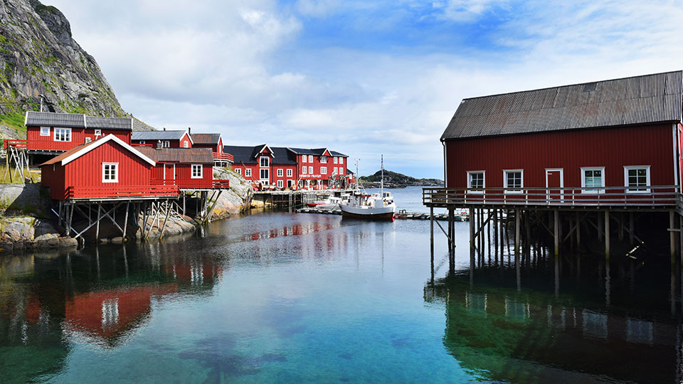 Les cabanes de pêcheurs rouges traditionnelles (rorbu) sur pilotis se reflétant dans les eaux calmes d'un port des îles Lofoten.